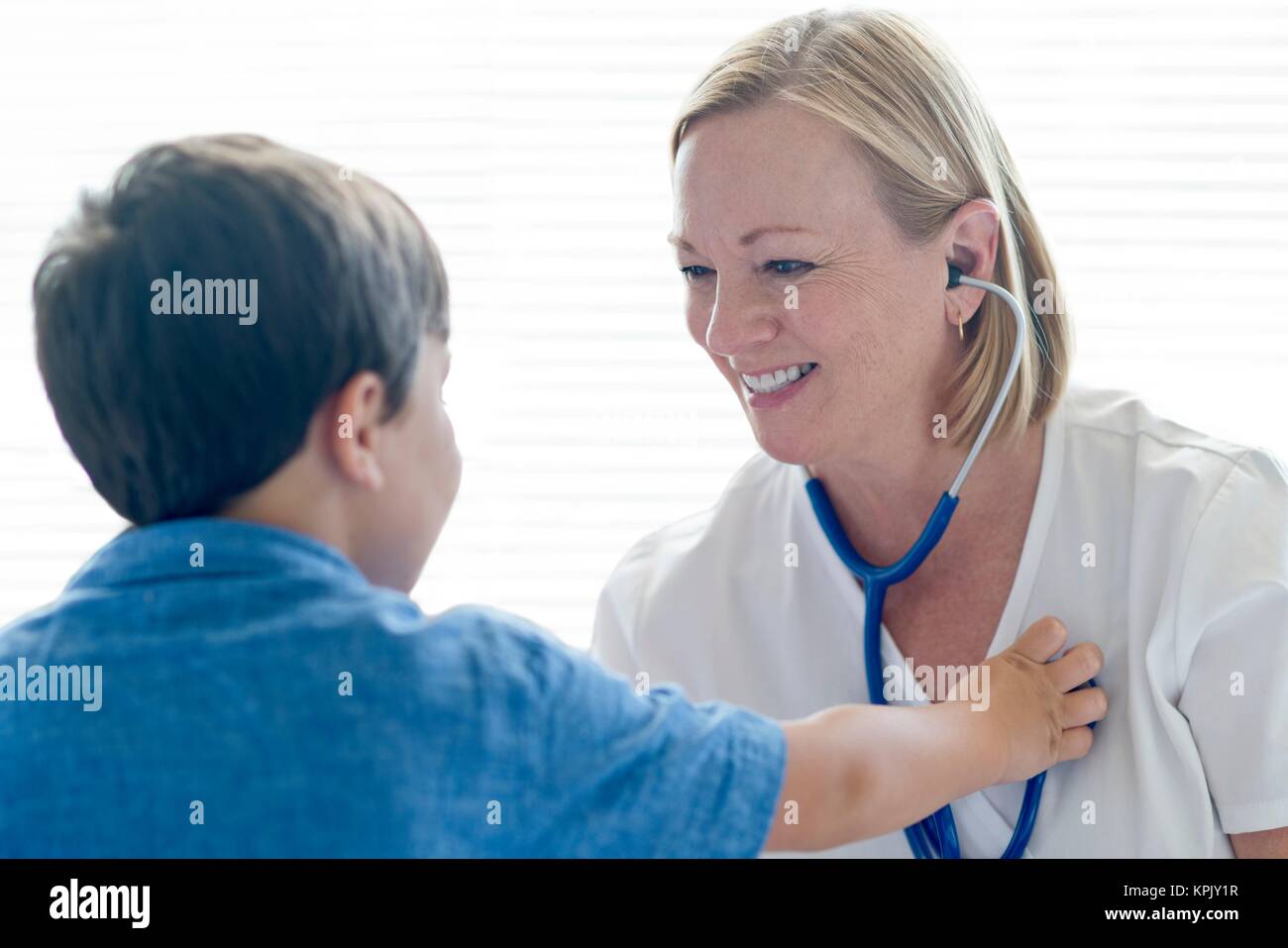 Nurse wearing stethoscope smiling towards young boy. Stock Photo