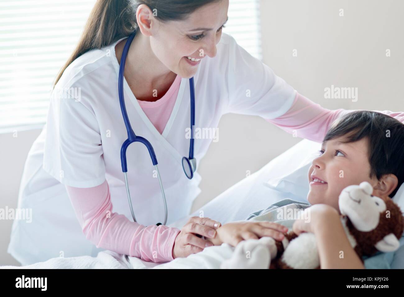 Young boy in hospital bed smiling towards female nurse. Stock Photo