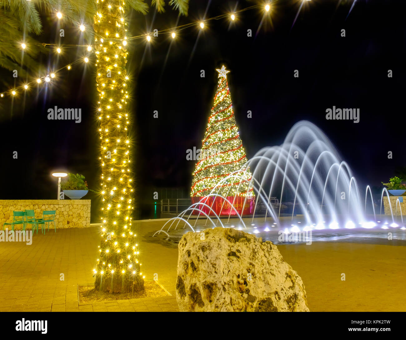 A Christmas tree, a water fountain and an illuminated palm tree with strip lights on a pedestrian street of Camana Bay, Grand Cayman, Cayman Islands Stock Photo