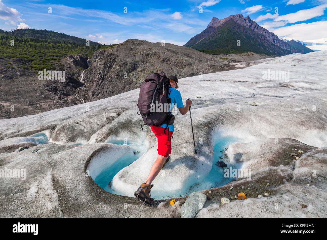 A backpacker crosses a stream on the surface of Root Glacier in Wrangell-St. Elias National Park. Donoho Peak is in the background Stock Photo