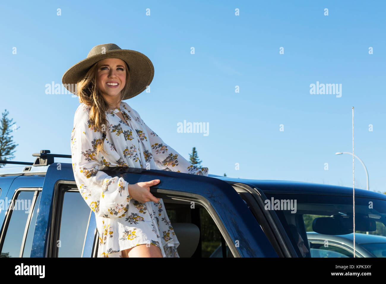 Young woman with long blond hair and hat posing for the camera at the open door of a vehicle; Edmonton, Alberta, Canada Stock Photo