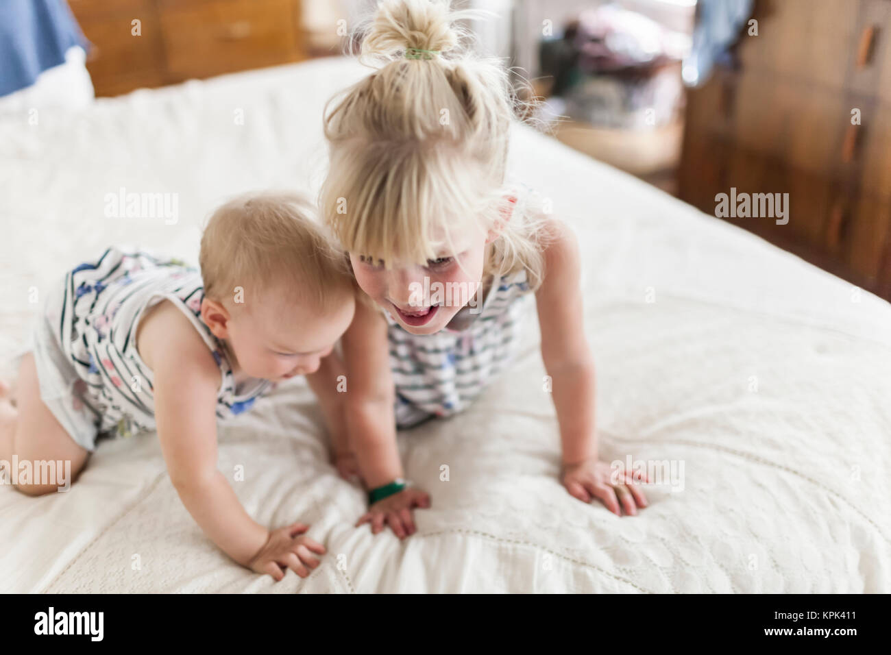 Two sisters, a baby and a toddler, play together on a bed; Sorrento, British Columbia, Canada Stock Photo