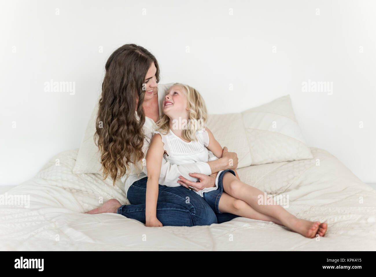 Portrait of a mother and young daughter sitting on a bed spending time together; Sorrento, British Columbia, Canada Stock Photo