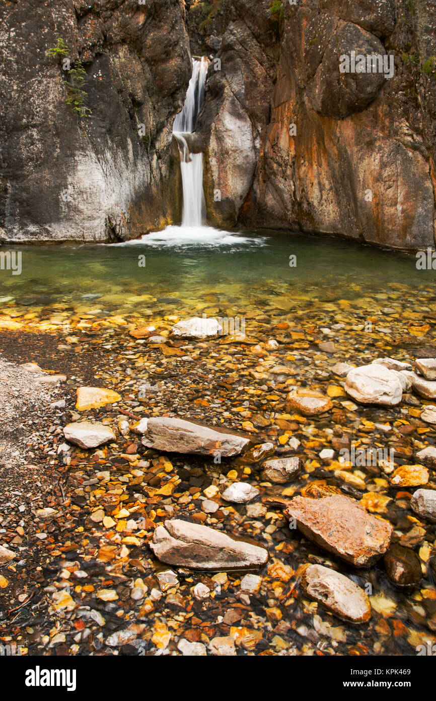 A double waterfall between dark rock walls with the foreground of colourful small rocks and pebbles; Calgary, Alberta, Canada Stock Photo