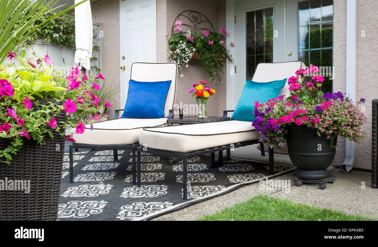 A patio at the back of a residence with two lounge chairs and pots of lush colourful flowers; Surrey, British Columbia, Canada Stock Photo