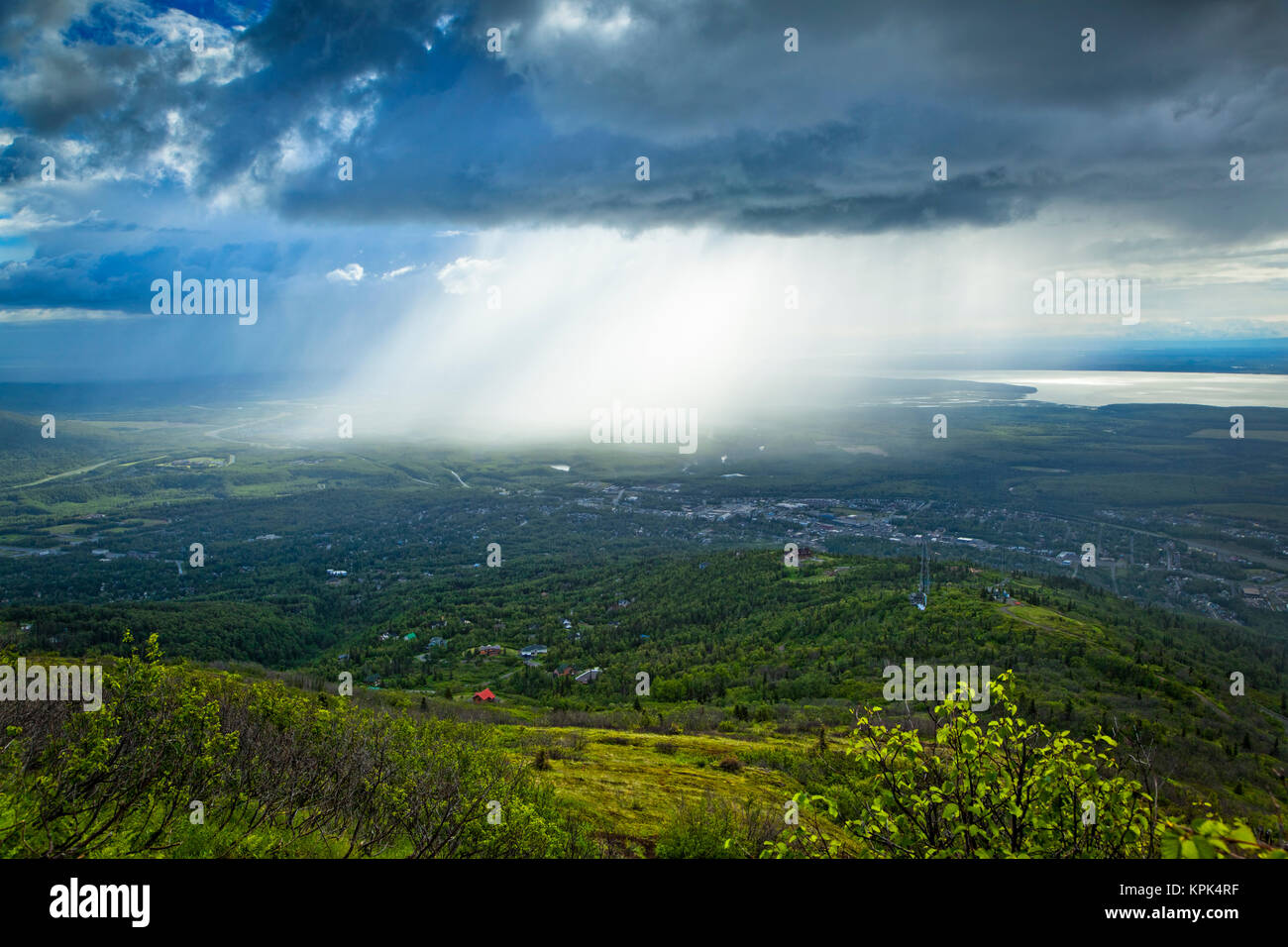 Rays of sunlight break through the dark clouds to the city below; Eagle River, Alaska, United States of America Stock Photo
