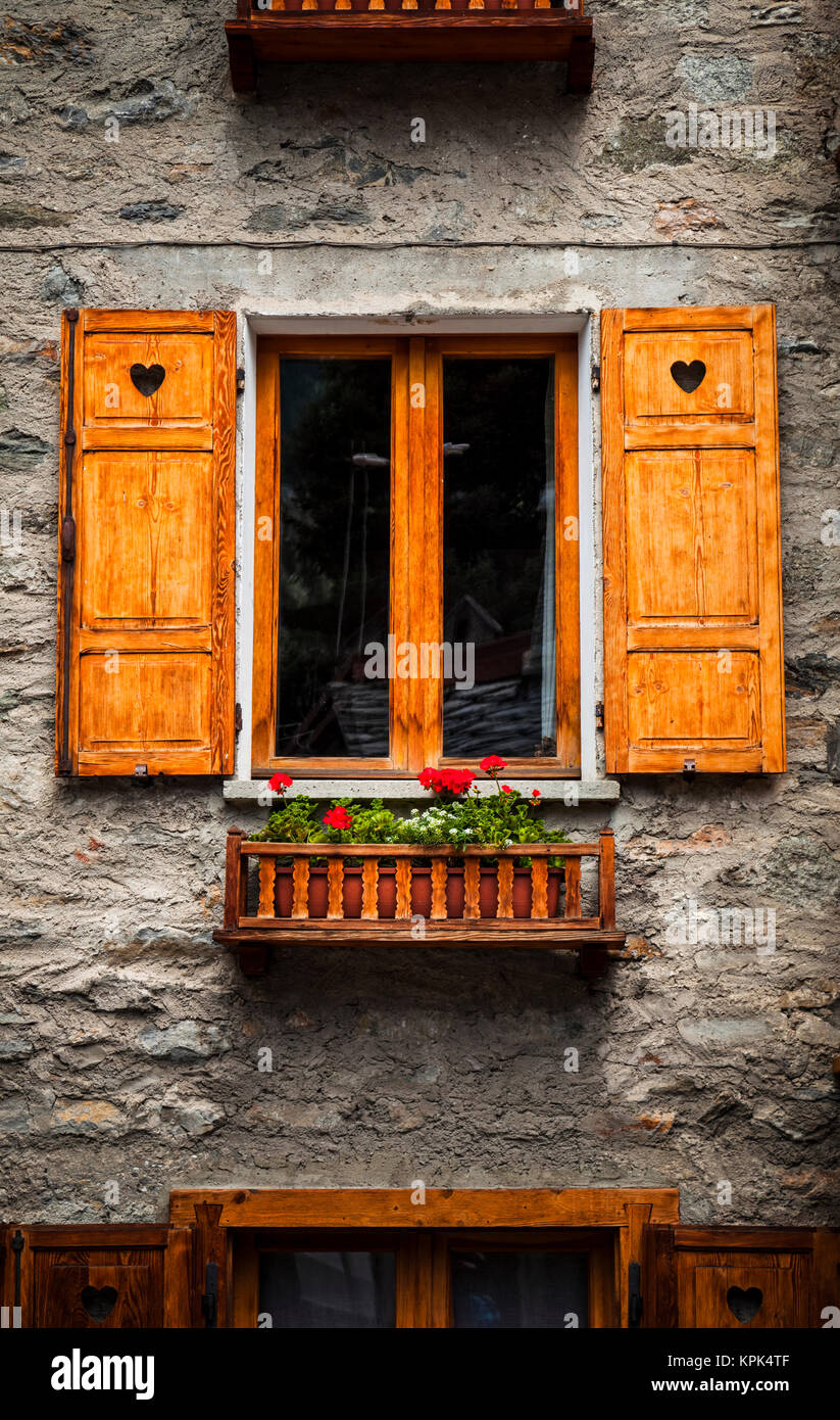 Wooden window shutters and flowers on a old stone building, near Courmayeur; Dolonne, Aosta Valley, Italy Stock Photo
