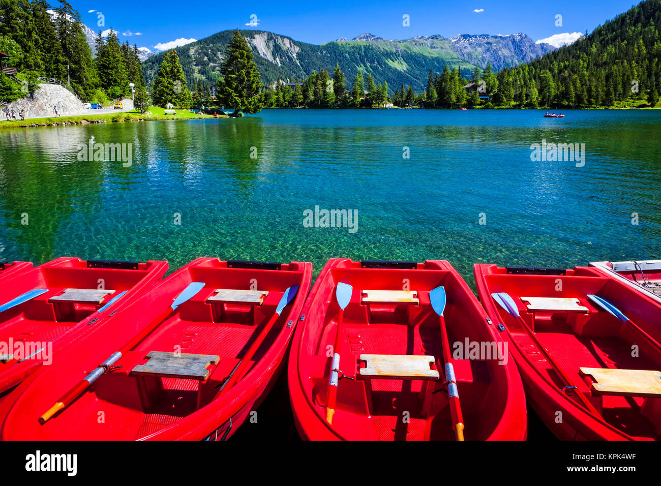 Red boats lined up at Champex Lake under blue sky with a mountain range in the background; Champex, Valais, Switzerland Stock Photo