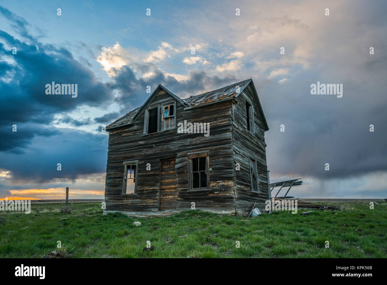 Abandoned house on the prairies with storm clouds overhead at sunset