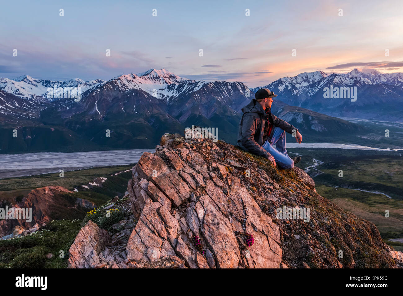 A man observes a tranquil sunset from an alpine perch in the Alaska Range high above the Delta River; Alaska, United States of America Stock Photo