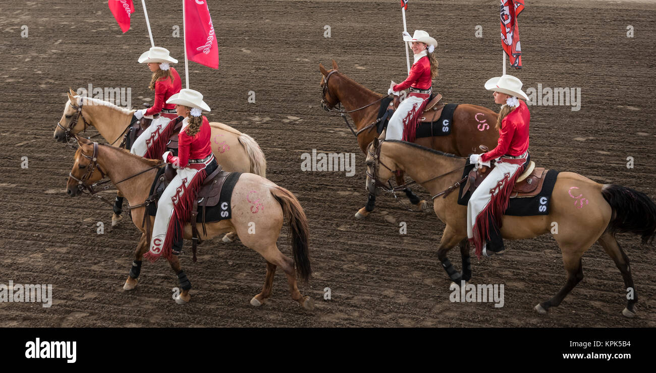 Cowgirls in red and white riding horses and carrying flags at the