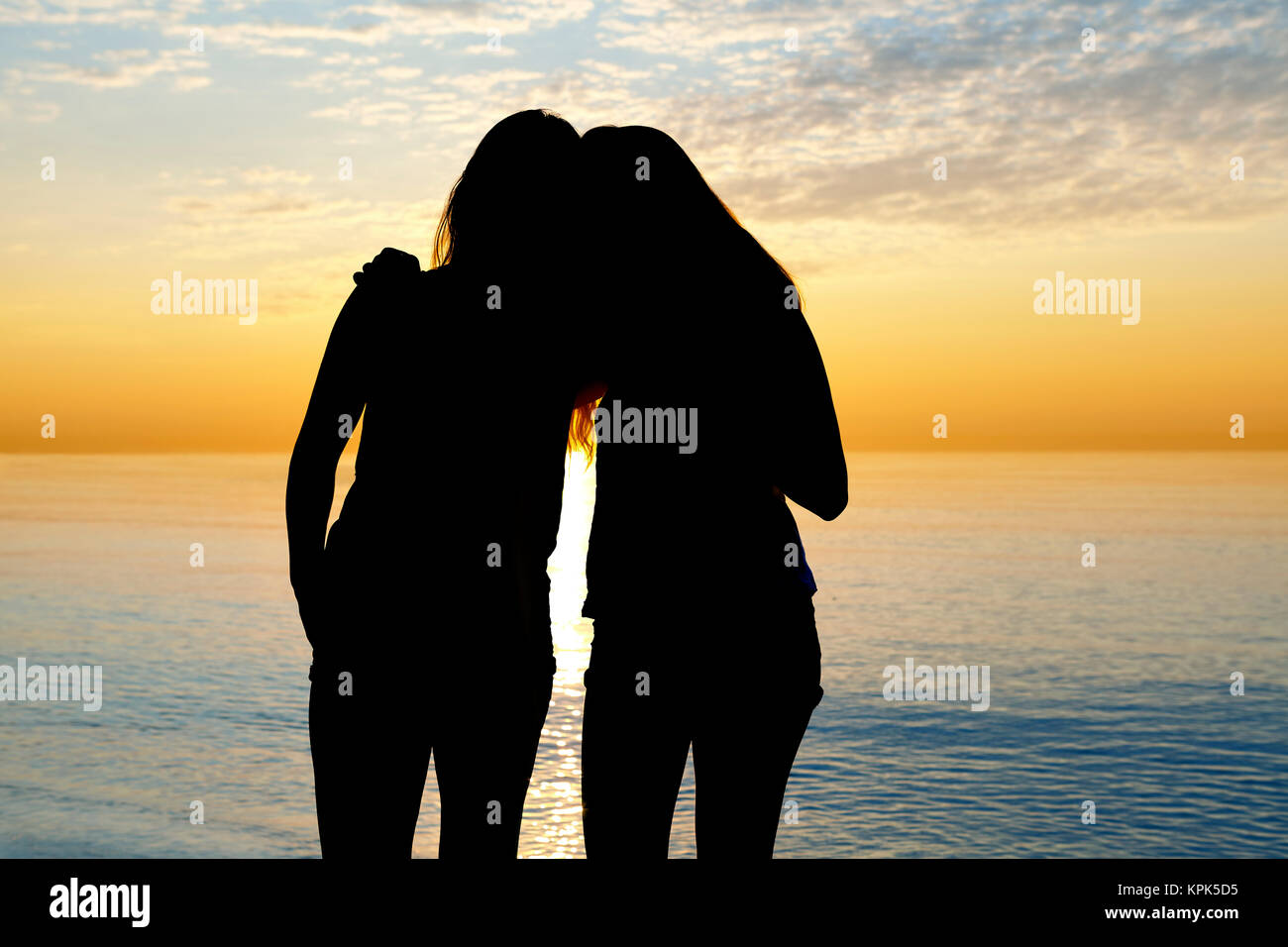 Silhouette of two teenage girls standing in an embrace looking out at a lake at sunset, Woodbine Beach; Toronto, Ontario, Canada Stock Photo
