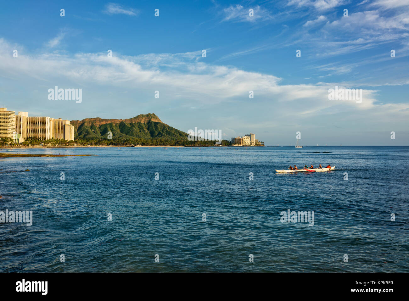 Tourists paddle in an outrigger canoe at Waikiki with Diamond Head in