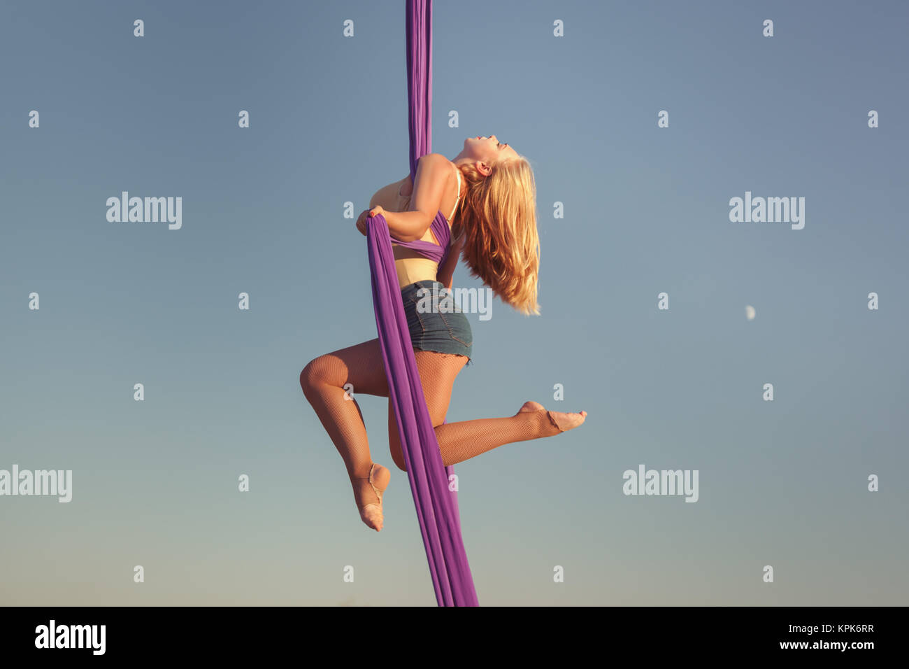 Air acrobat hangs on ropes high against the sky. Stock Photo