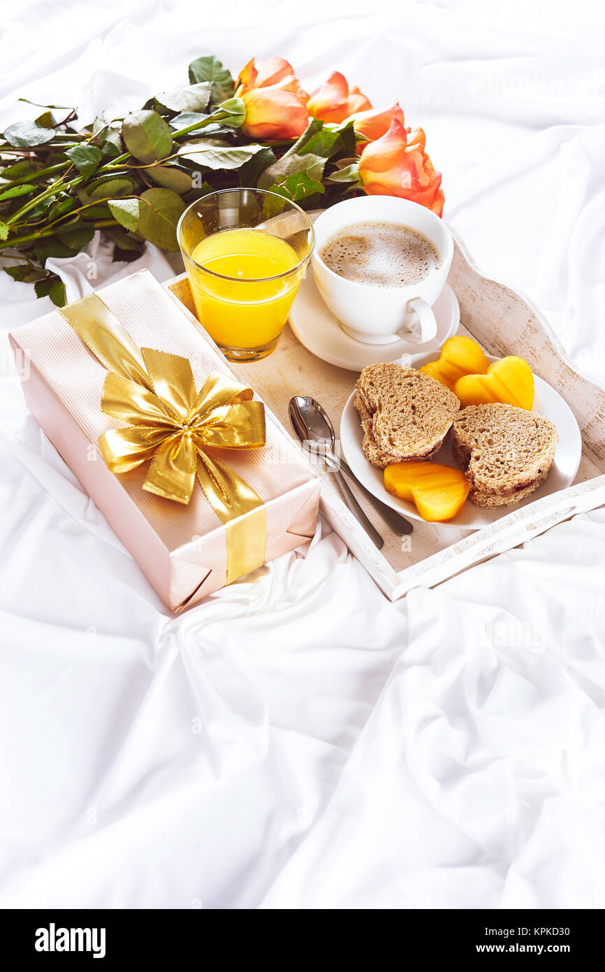 Vertical shot of tray with breakfast, present gift and roses in bed for