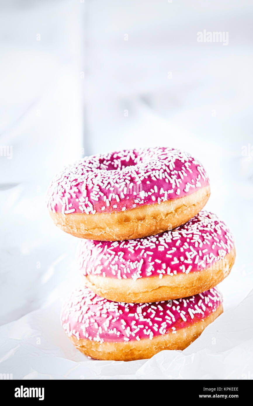 Stack of three colorful pink glazed ring doughnuts with sprinkles for a ...