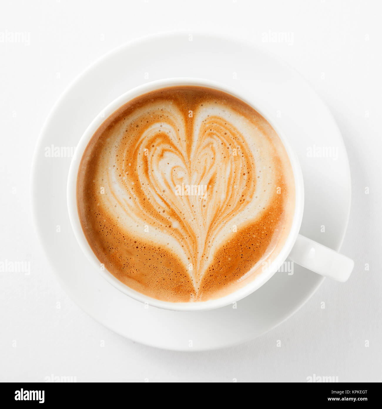 Cup of cappuccino coffee with a heart shape in the milky foam on top viewed from above in a generic white cup and saucer on white Stock Photo