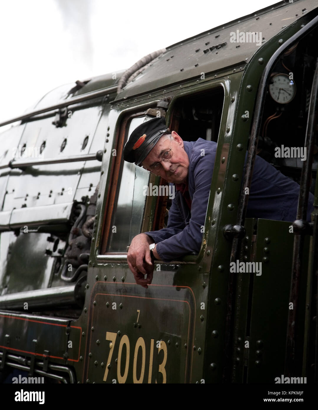 The driver of preserved British Railways Standard Class 7 steam locomotive no. 70013 Oliver Cromwell leaning out of his cab window. Stock Photo