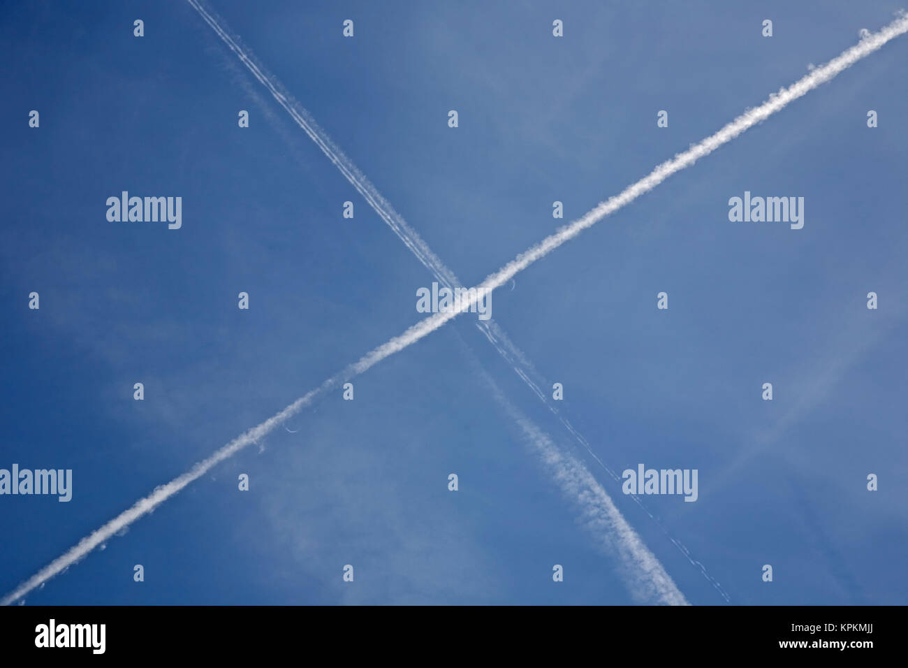 Aircraft vapour trails or contrails across a blue sky, forming a rough St Andrew's cross. Stock Photo