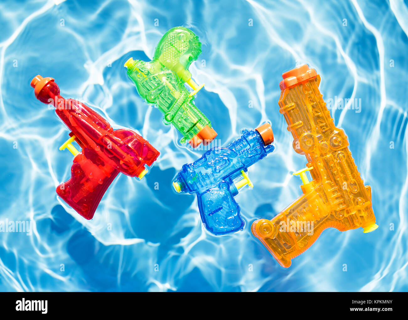Four colorful squirt guns floating in water. Stock Photo