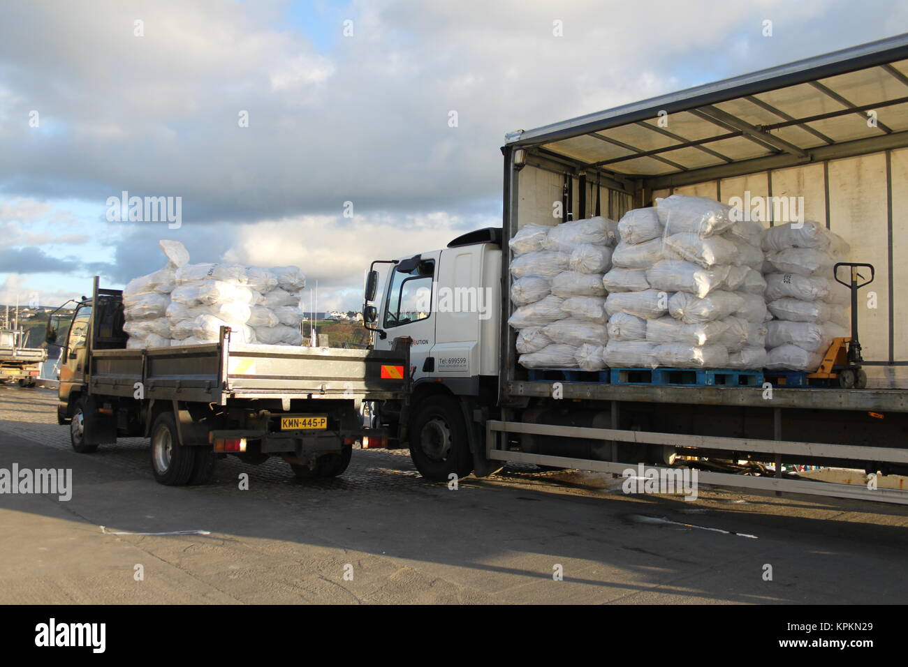 Pick up truk delivering sacks of scallops to a lorry at the harbourside, Peel, Isle of Man, British Isles. Fishing boats/trawlers in the background. Stock Photo