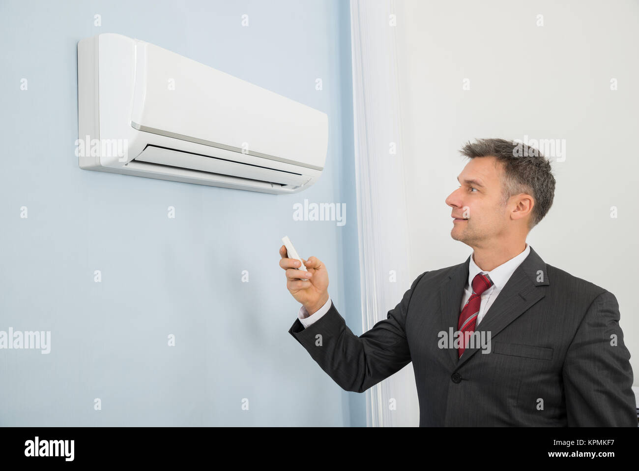 Businessman Using Remote Control To Operate Air Conditioner Stock Photo
