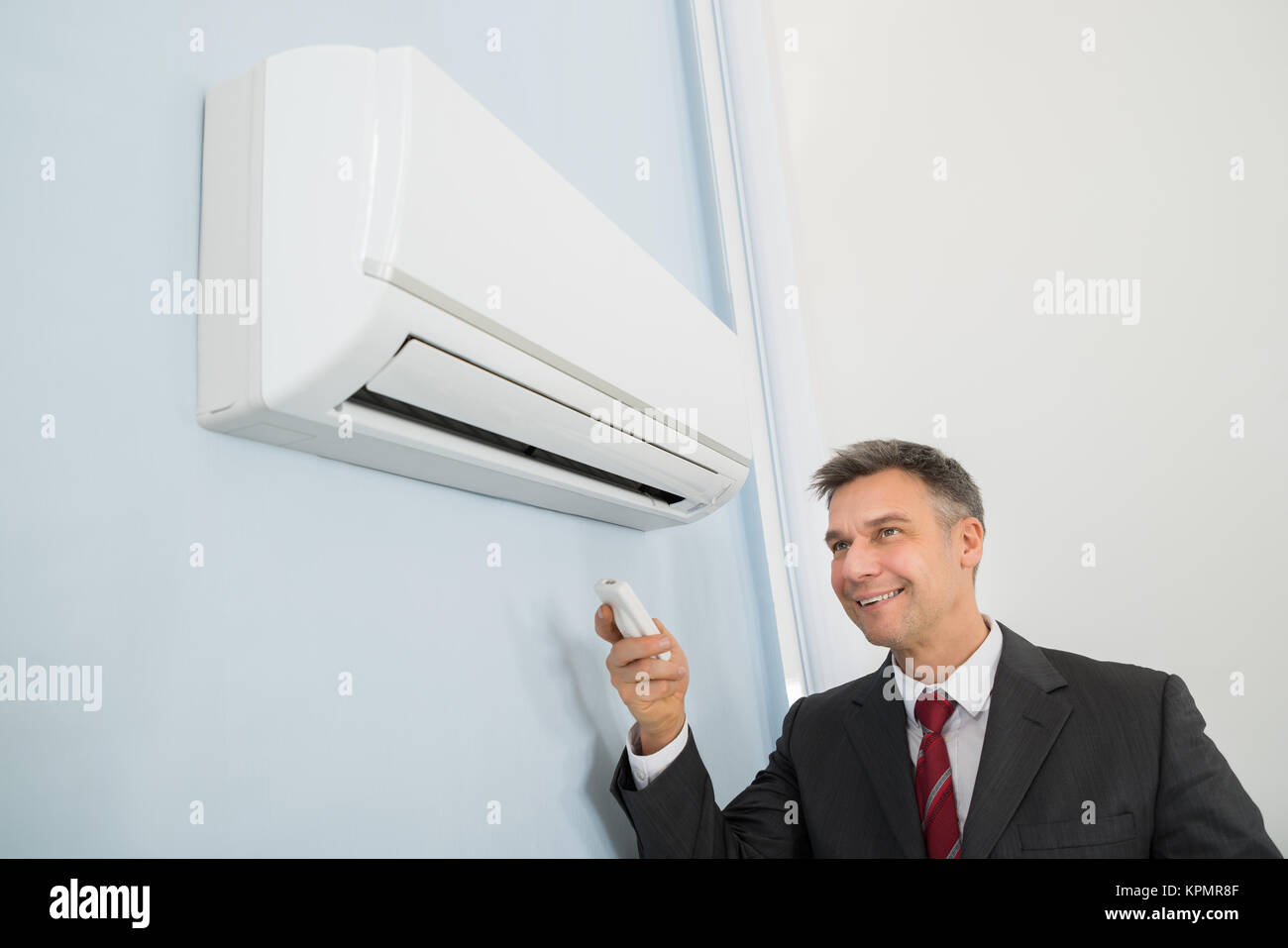 Businessman Using Remote Control To Operate Air Conditioner Stock Photo