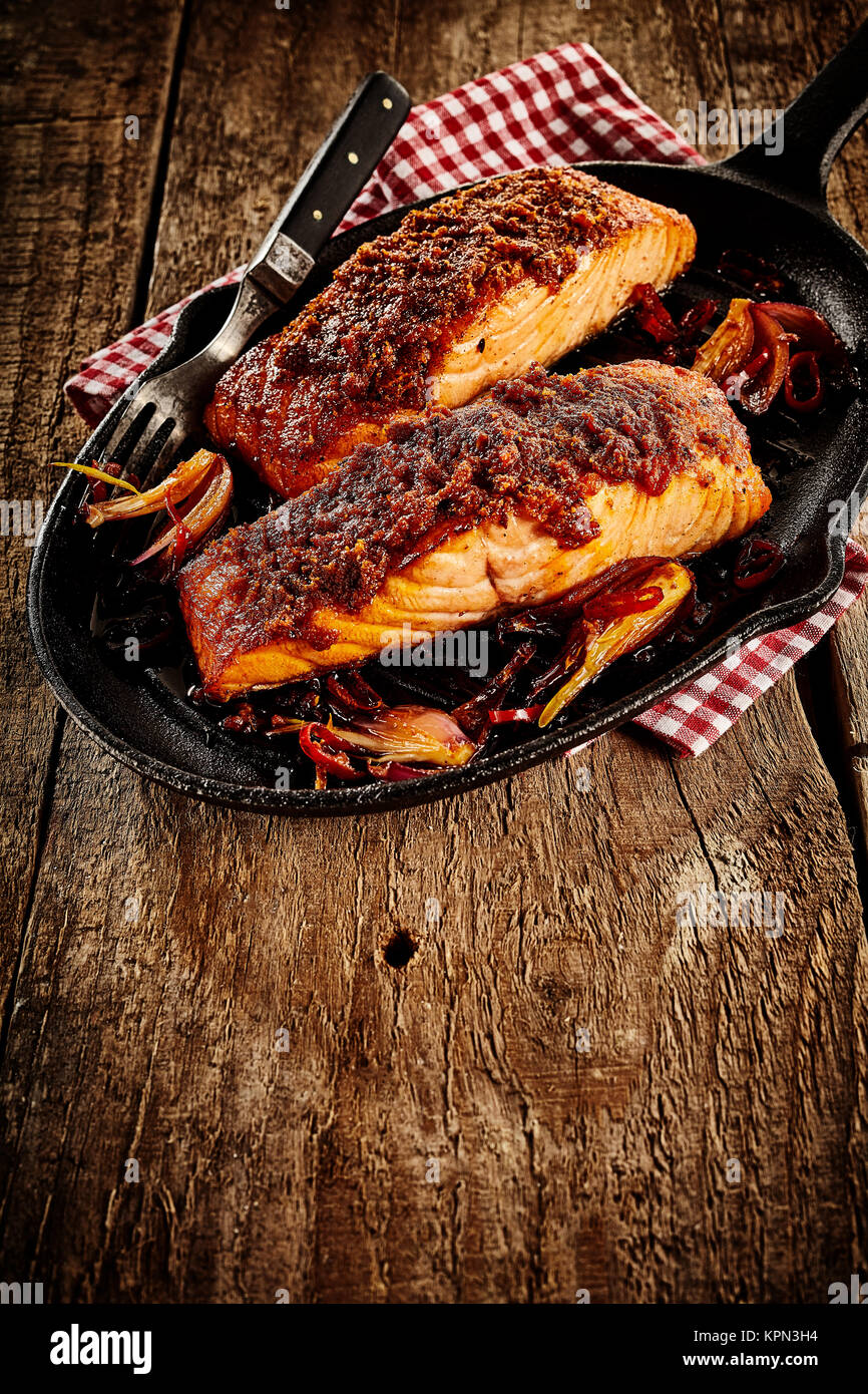 Spicy Mexican style baked salmon with sliced onions and fork in black