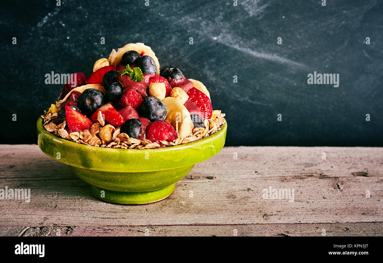 Nutritious giant ceramic green bowl of oats, blueberries, bananas, strawberry on wooden table with copy space and dark background Stock Photo