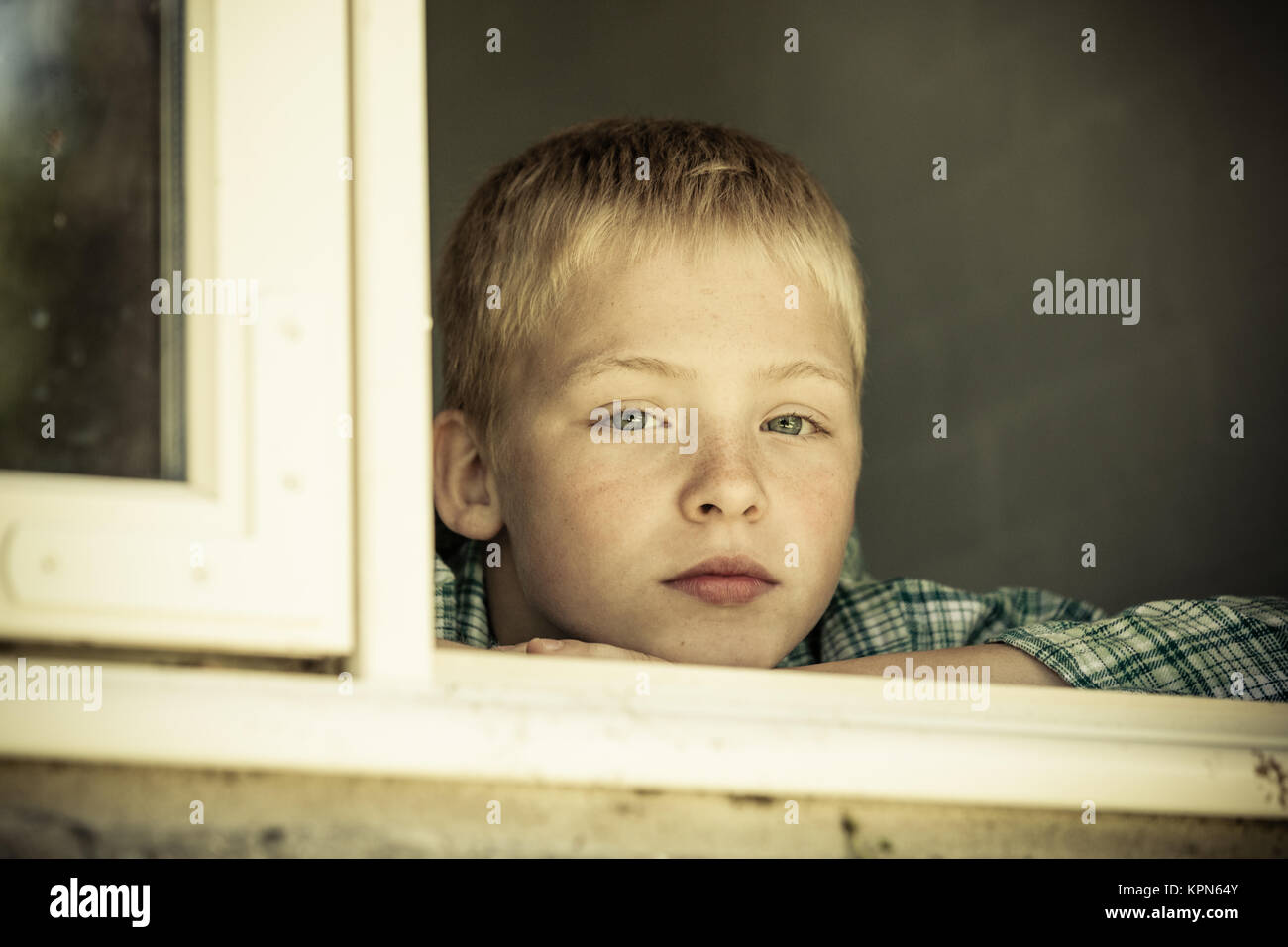 Child with sad expression looking out from window Stock Photo