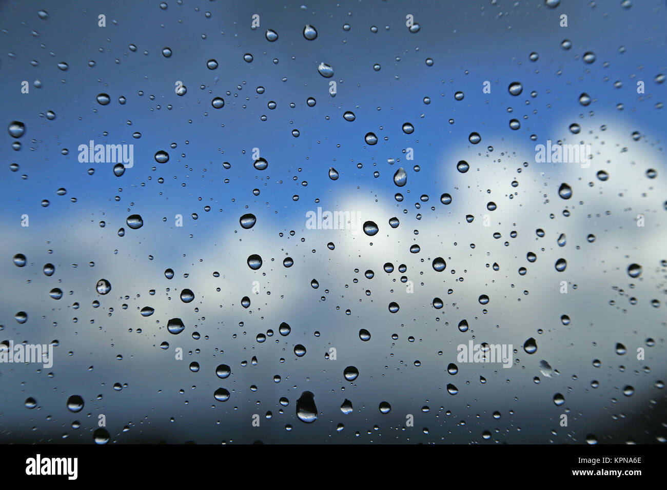 Regentropfen auf einer Fensterscheibe vor einem blauen Himmel mit Wolken Stock Photo