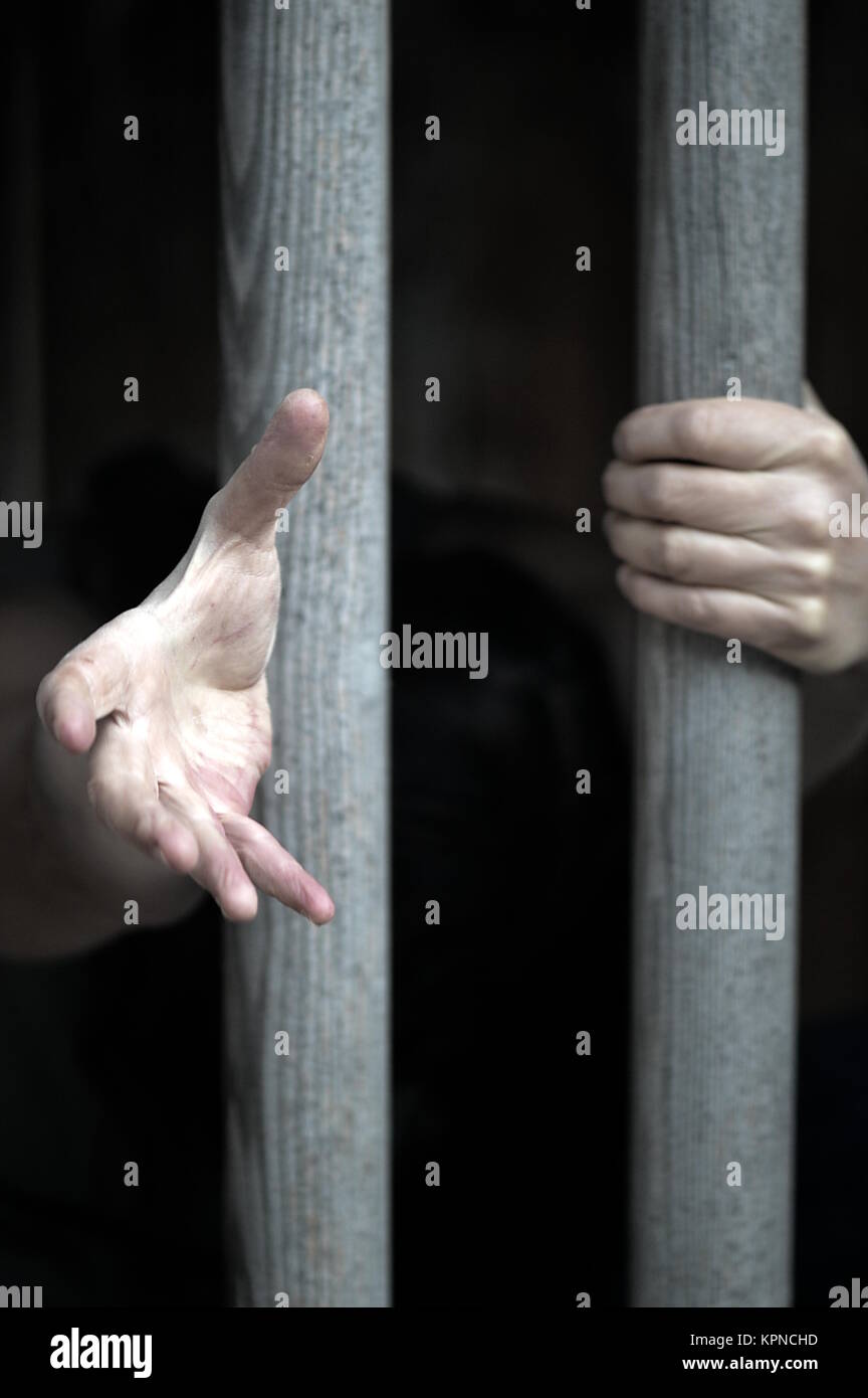 prisoner behind bars extends his hand pleading for help Stock Photo