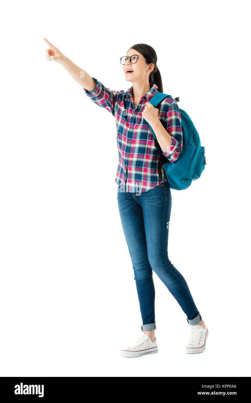 cheerful beautiful girl traveler standing on white background pointing empty area and holding personal baggage bag ready to travel. Stock Photo