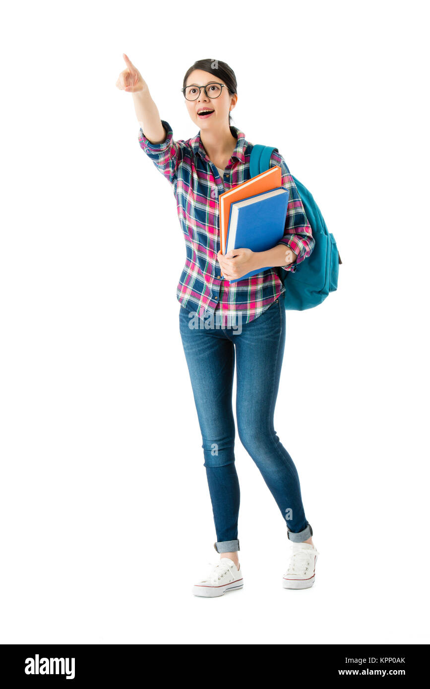 happy elegant female college student carrying school bag and holding studying book pointing blank area isolated on white background. Stock Photo