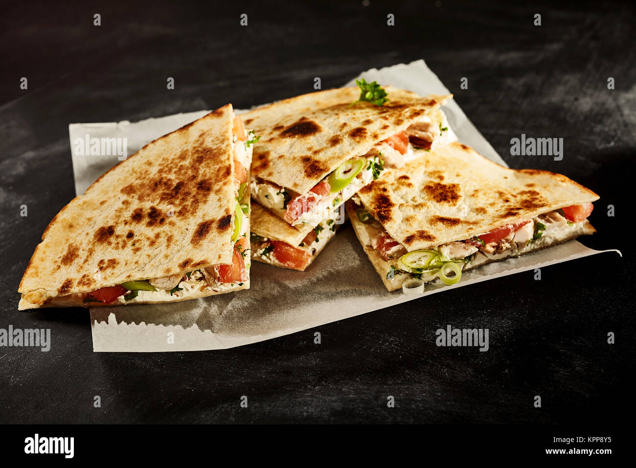 Set of four nutrious cooked chicken wheat tortilla quesadillas stuffed with onion, tomato and herbs in wax paper on dark table Stock Photo