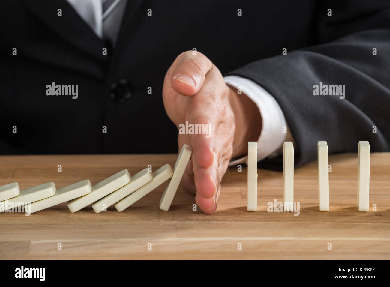 Businessman Stopping Dominoes From Falling Stock Photo - Alamy