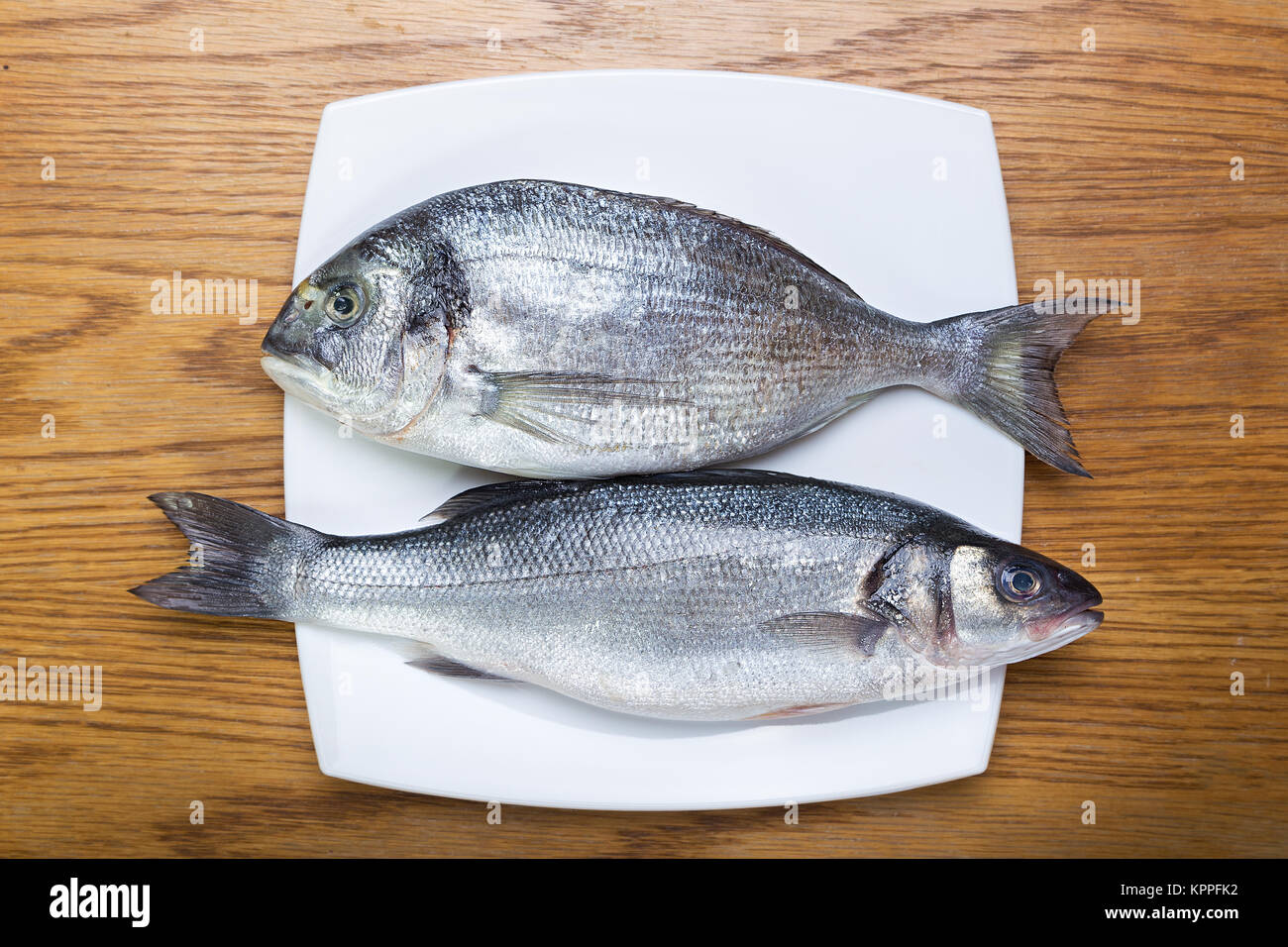 fresh raw fish sea bass and sea bream on a white plate on a wooden table  Stock Photo - Alamy