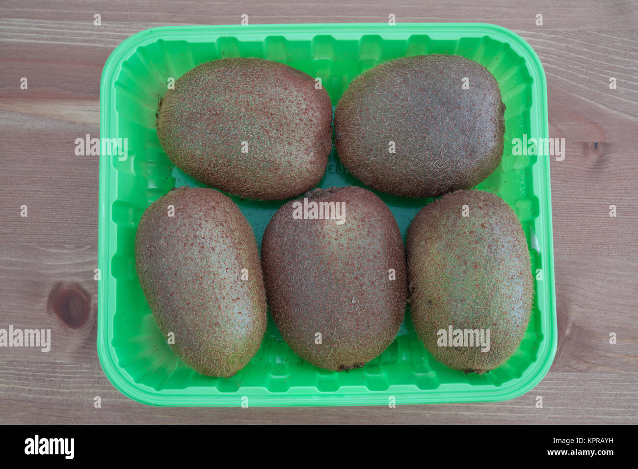 Five Kiwi fruits in a green box isolated on wooden background Stock Photo