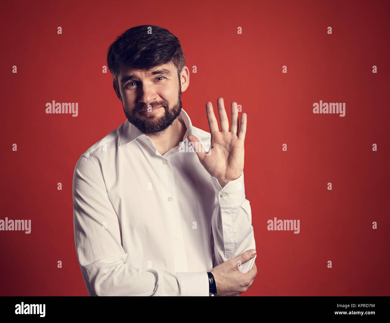 Happy smiling bearded businessman waving the hand and saying hello in fashion white style shirt on dark red background. Closeup toned portrait Stock Photo