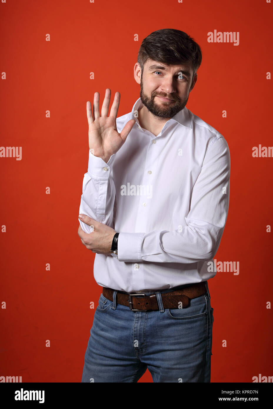Happy smiling bearded businessman waving the hand and saying hello in fashion white style shirt on bright orange background. Closeup portrait Stock Photo