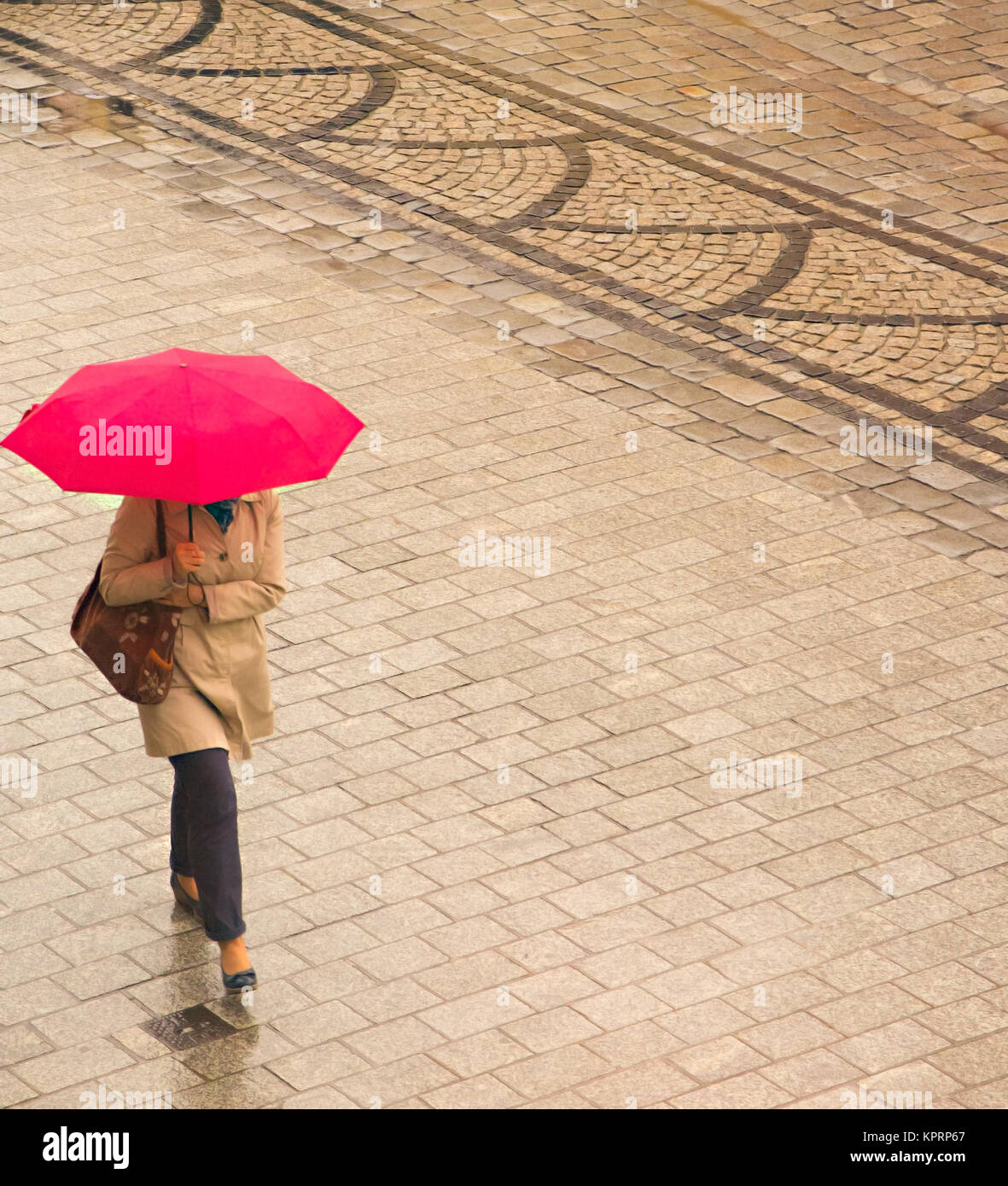 Woman walking in the rain under bright red umbrella / parasol  in the market square in the Polish city of Wroclaw Poland Stock Photo