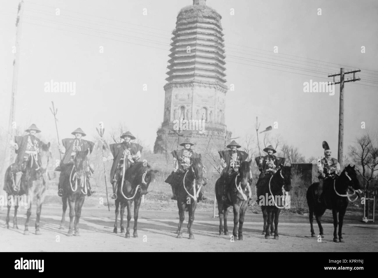 7 Chinese Gendarmes in peaked hats are mounted as skirmishes as cavalry in front of a temple. Stock Photo