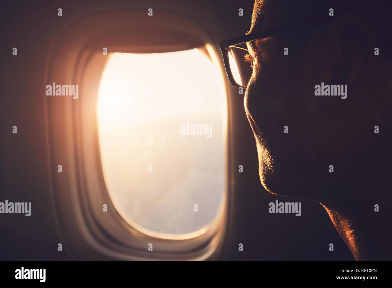 Young passenger looking out through window of the airplane during sunrise. Stock Photo