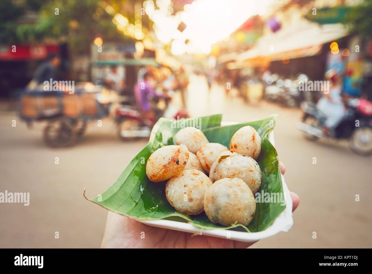 Hand of man holding bowl with sweet coconut food. Busy street full of restaurants, bars and shops - Siem Reap, Cambodia Stock Photo