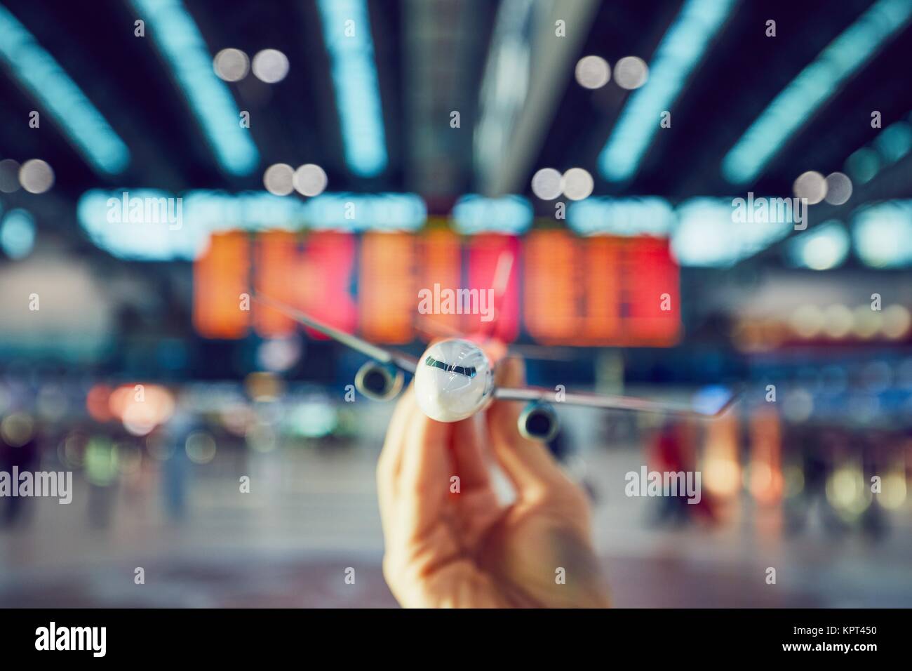 Hand is holding model airplane against arrival and departure board in a airport terminal. Stock Photo