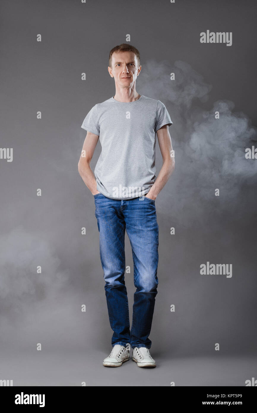 Middle age man in jeans with hands in pockets and t-shirt on gray background Stock Photo