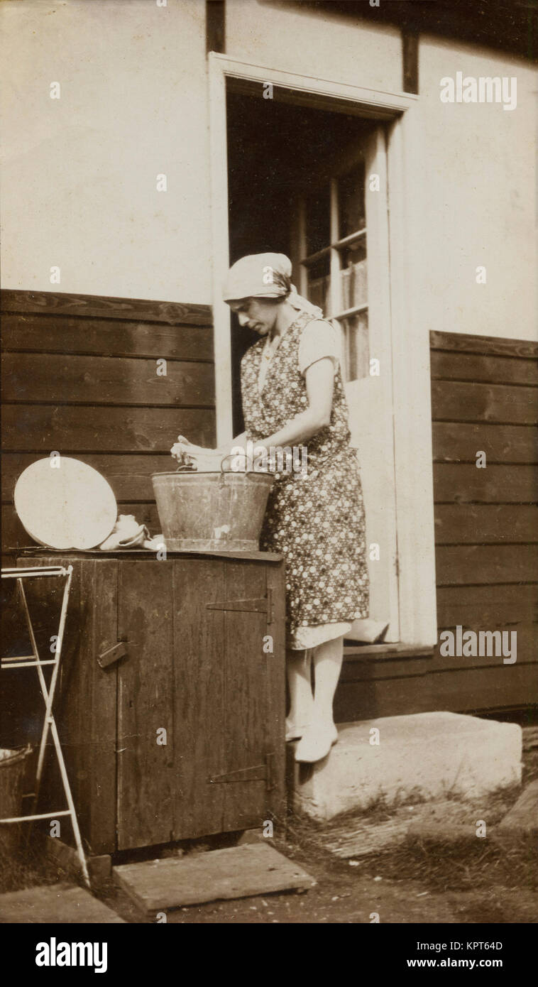 1930s, a woman doing her washing by-hand using a tin bucket on the backstep at the rear of her home. Stock Photo