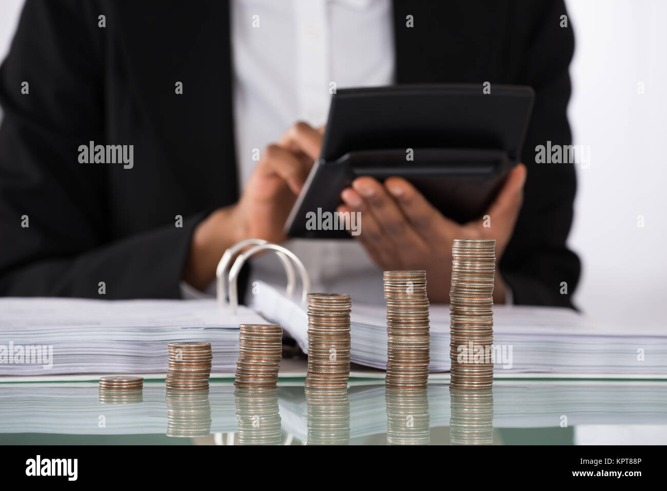 Businesswoman Calculating Invoice With Coins On Desk Stock Photo