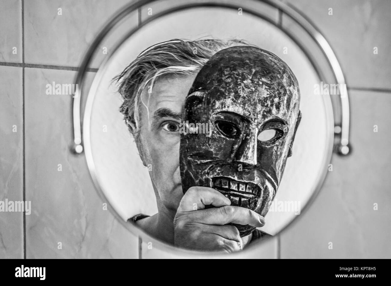 Mann mit Maske betrachtet sich im Spiegel. Stock Photo