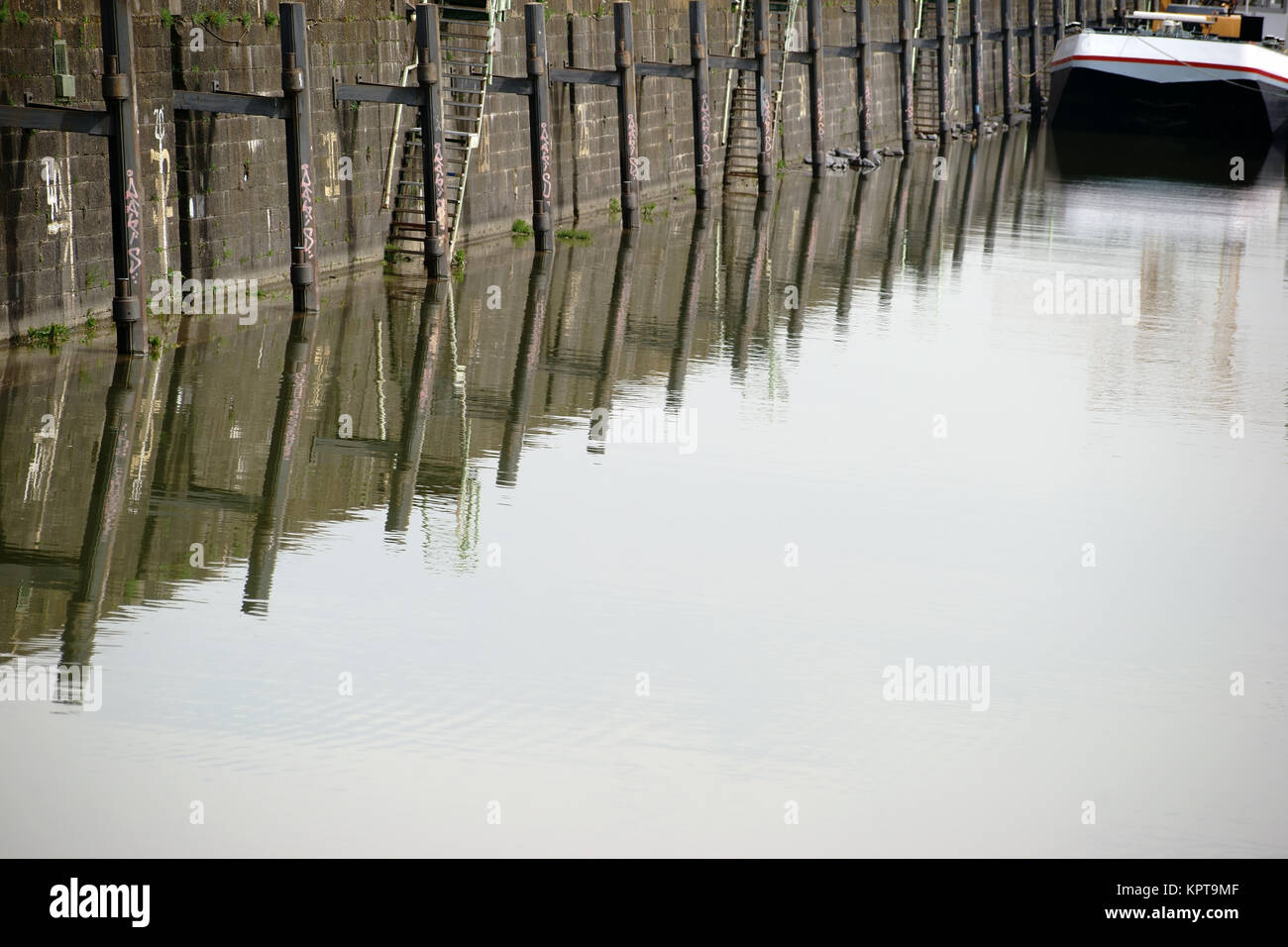 Die Pfeiler einer Schiffanlegestelle spiegeln sich im Wasser eines Hafenbeckens. Stock Photo